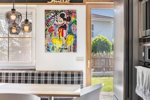 A modern kitchen with a stainless steel refrigerator, a wooden bench, and a colorful painting of a cartoon character.