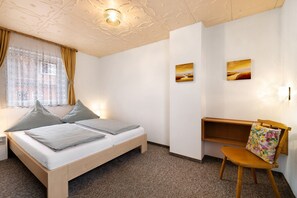Een slaapkamer met een bed, nachtkastje, houten stoel en plank.