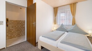 A bedroom with a bed, a nightstand, a window with curtains, and a door leading to a bathroom. - Apartment '4' with Wi-Fi (Lindau)