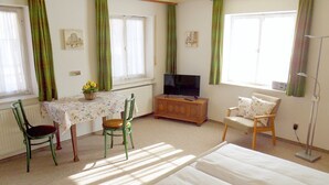 Una habitación con una cama, una mesa con sillas, un televisor y una ventana con cortinas.