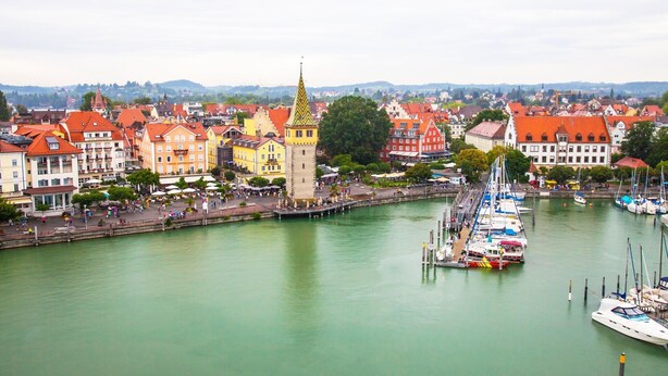 A riverside town with historic buildings, a prominent tower, and a marina with boats.