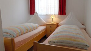A twin room with two single beds, a nightstand with a lamp, and a window with red curtains.