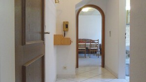 A hallway with a tiled floor, a wooden door, a telephone, and a dining area with chairs and a table.