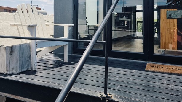 Een modern gebouw met grote glasramen, een metalen hekwerk en een houten terras.