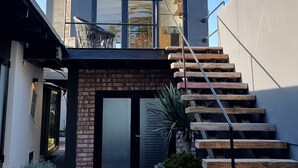 Een modern huis met twee verdiepingen, voorzien van een glazen deur, een houten trap en een kleine tuin met planten.