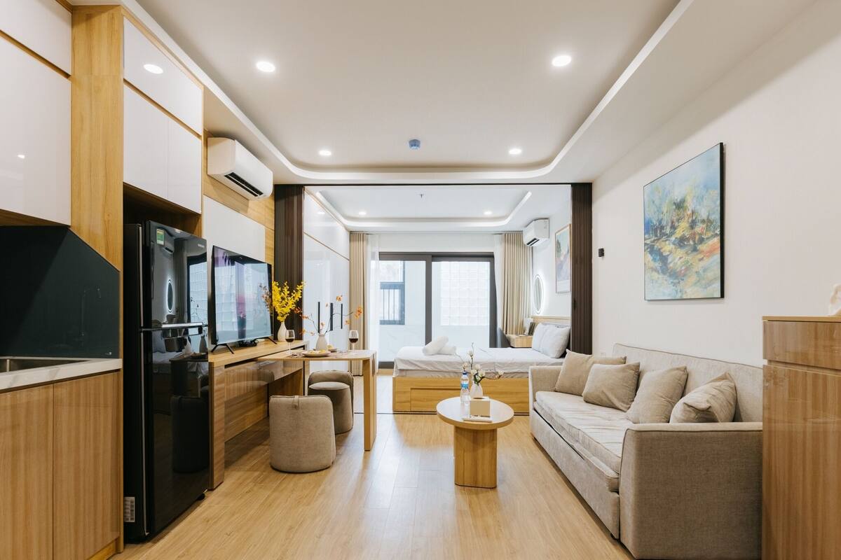 Una habitación de hotel moderna con kitchenette, un sofá, una mesa de centro y un ventanal grande.