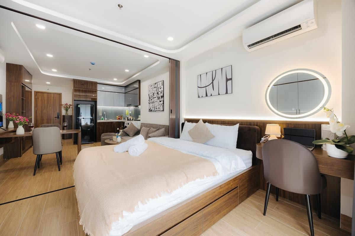 Habitación de hotel moderna con una cama grande, un escritorio, una silla y un espejo redondo con iluminación integrada.