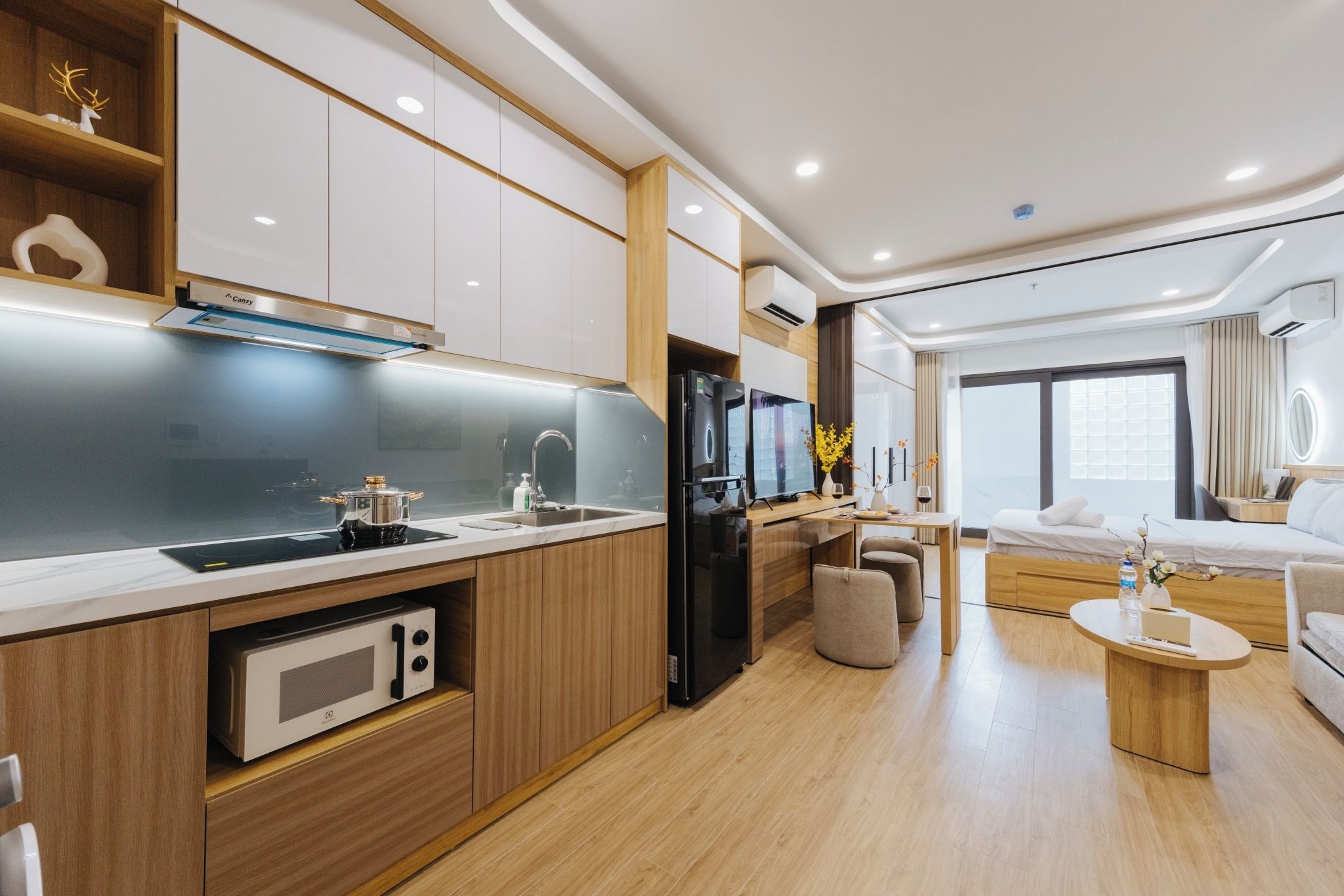 Une cuisine moderne équipée d’un four, d’un micro-ondes et d’un réfrigérateur encastrés. On y trouve également un coin repas avec une table et des chaises, ainsi qu’une chambre à coucher avec un lit et une fenêtre.