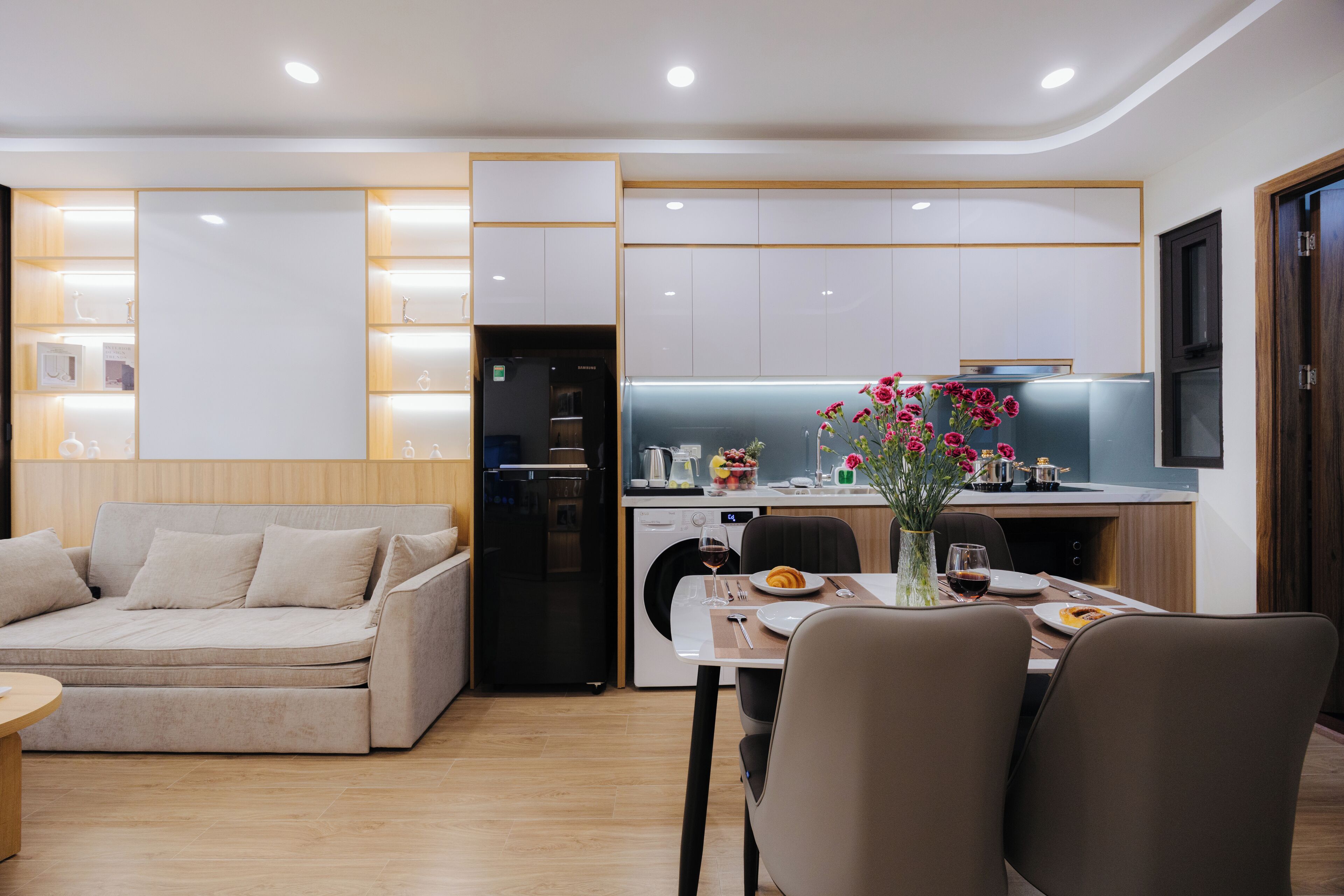 A modern kitchen with built-in appliances, a dining area with a table set for two, and a sofa in the living area.