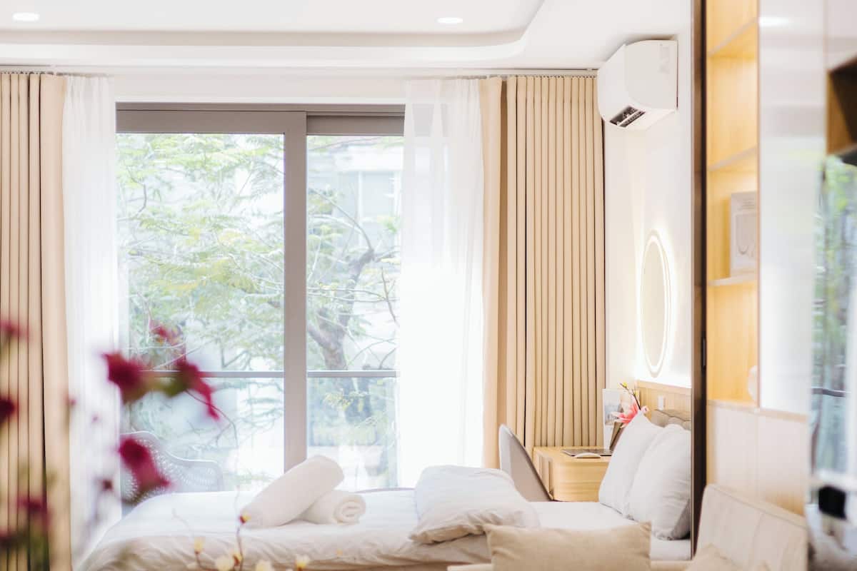 Una habitación de hotel moderna con cama, sofá, una mesita redonda con un plato y una copa de vino, y un amplio ventanal con cortinas.