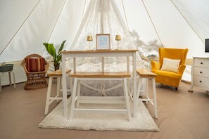 Une pièce aménagée avec une tente, une table centrale, un fauteuil jaune, une chaise en osier et une petite table d’appoint avec une lampe.