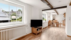 A modern kitchen with a large window, wooden flooring, and a dining area with chairs and a table. - Holiday Apartment '5, 75sqm' with Shared Terrace, Shared Garden and Wi-Fi (Schmallenberg)