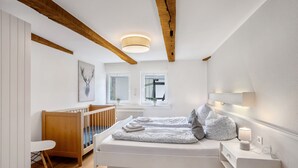 A modern bedroom with a wooden ceiling, a crib, a bed with pillows, and a bedside table with a lamp. - Holiday Apartment '5, 75sqm' with Shared Terrace, Shared Garden and Wi-Fi (Schmallenberg)