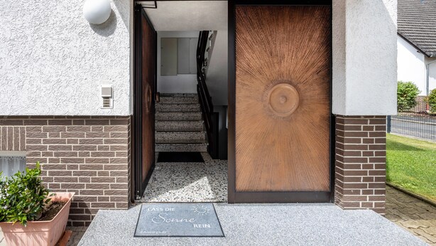 A modern building entrance with a wooden door, a staircase, and a potted plant. - Holiday Apartment 'Waldmann' with Shared Terrace, Garden, and Wi-Fi (Hattorf am Harz)