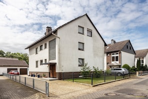 Um edifício residencial de dois andares com garagem, quintal cercado e entrada pavimentada.