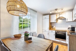 A modern kitchen with white cabinets, a built-in oven, and a dining area with a wooden table and chairs. - Holiday Apartment '2, 70sqm' with Shared Terrace, Shared Garden and Wi-Fi (Schmallenberg)