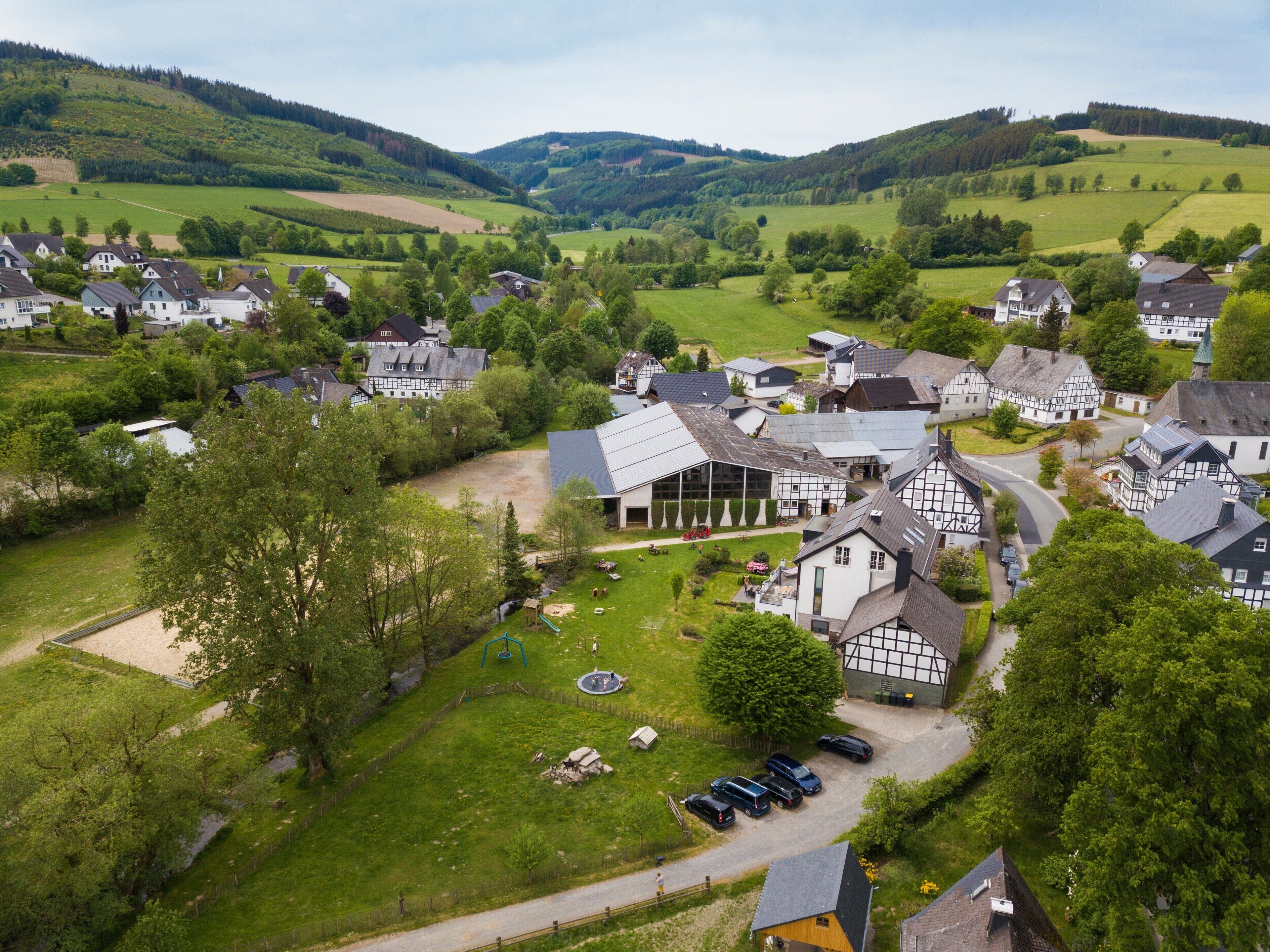 Un village rural avec des maisons traditionnelles à colombages, un bâtiment central doté d’un toit en pente et une aire de jeux.