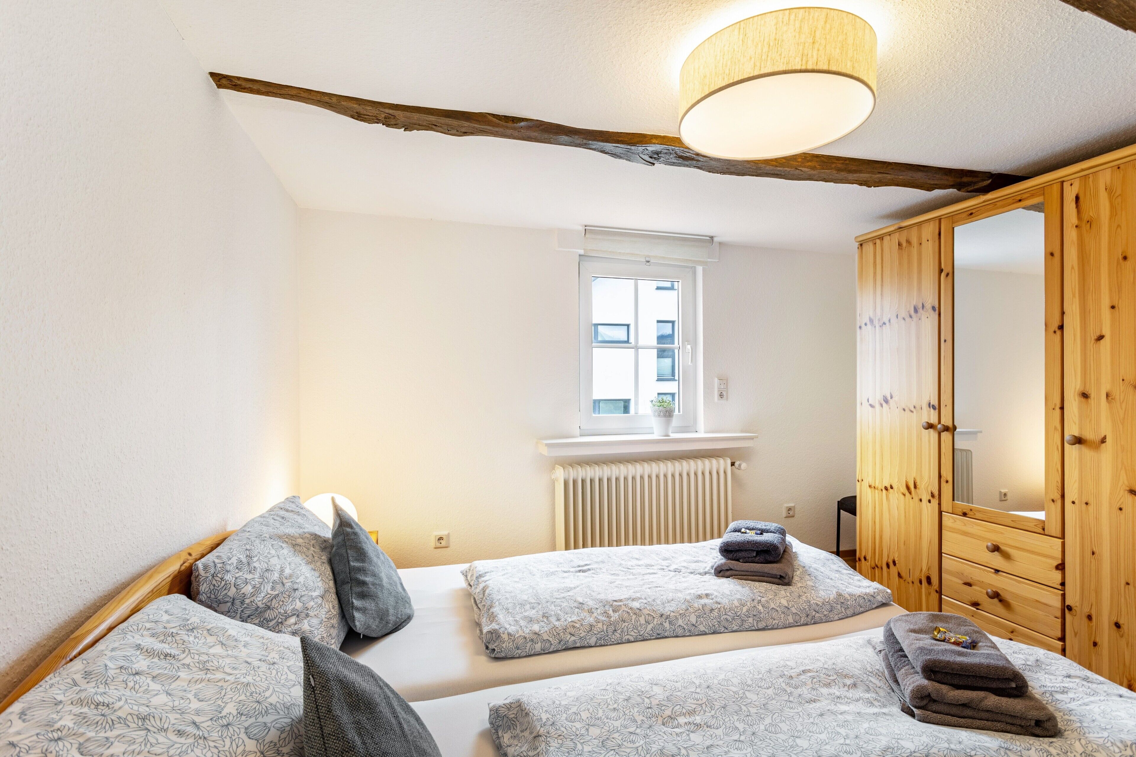 A bedroom with two beds, a wooden wardrobe, a window, and a radiator.