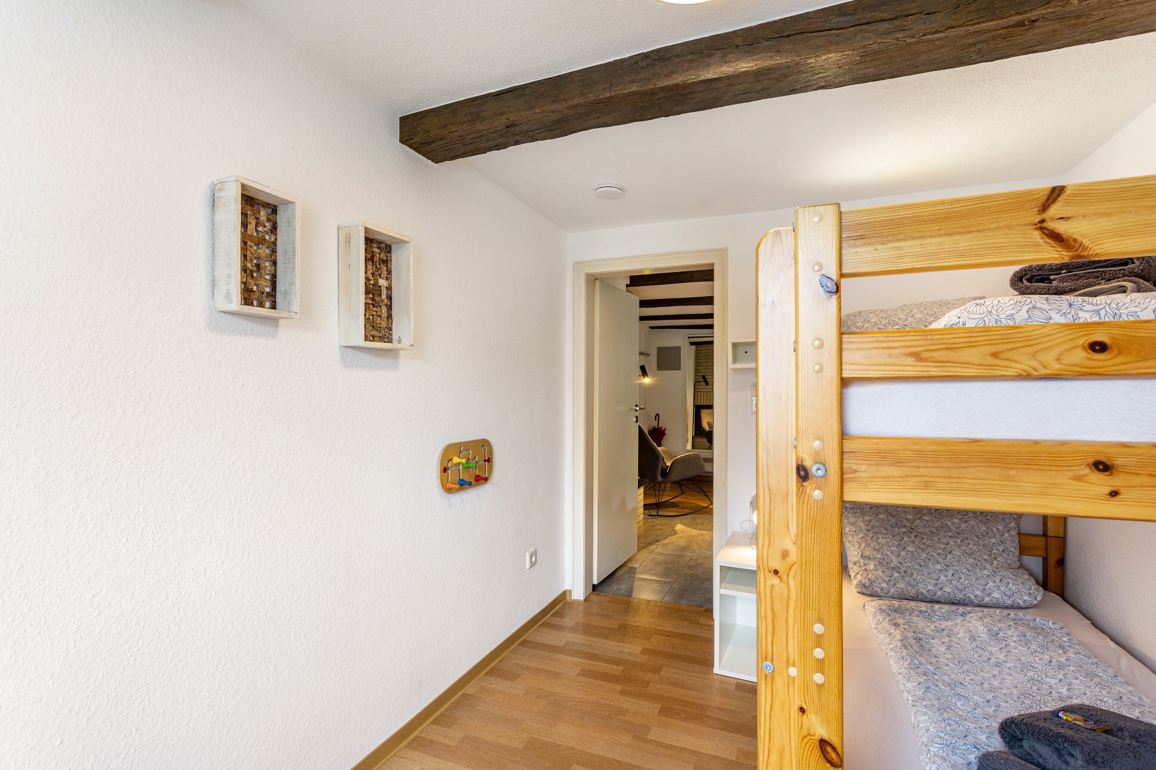 Ein Schlafraum mit Etagenbetten, Holzbalken, einer weißen Wand und einer Tür zu einem anderen Raum.