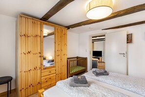 A bedroom with a wooden wardrobe, a crib, a bed with two pillows, a television, and a door leading to another room. - Holiday Apartment '3, 53sqm' with Shared Terrace, Shared Garden and Wi-Fi (Schmallenberg)