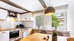 A modern kitchen with white cabinets, a wooden dining table, and a view of a tree outside. - Holiday Apartment '3, 53sqm' with Shared Terrace, Shared Garden and Wi-Fi (Schmallenberg)