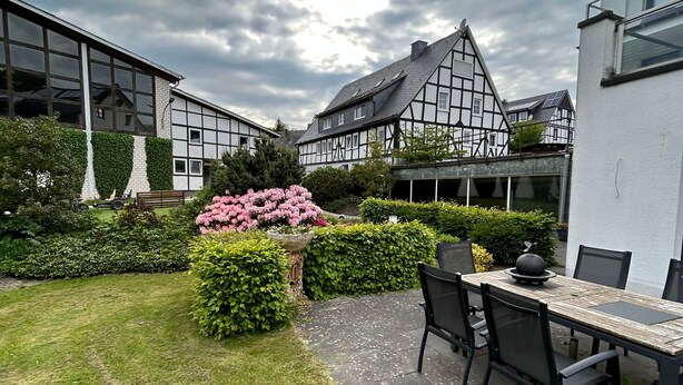 A courtyard with a dining area, a garden with pink flowers, and traditional and modern buildings. - Holiday Apartment '3, 53sqm' with Shared Terrace, Shared Garden and Wi-Fi (Schmallenberg)