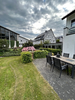 A courtyard with a dining area, a garden with pink flowers, and traditional and modern buildings.