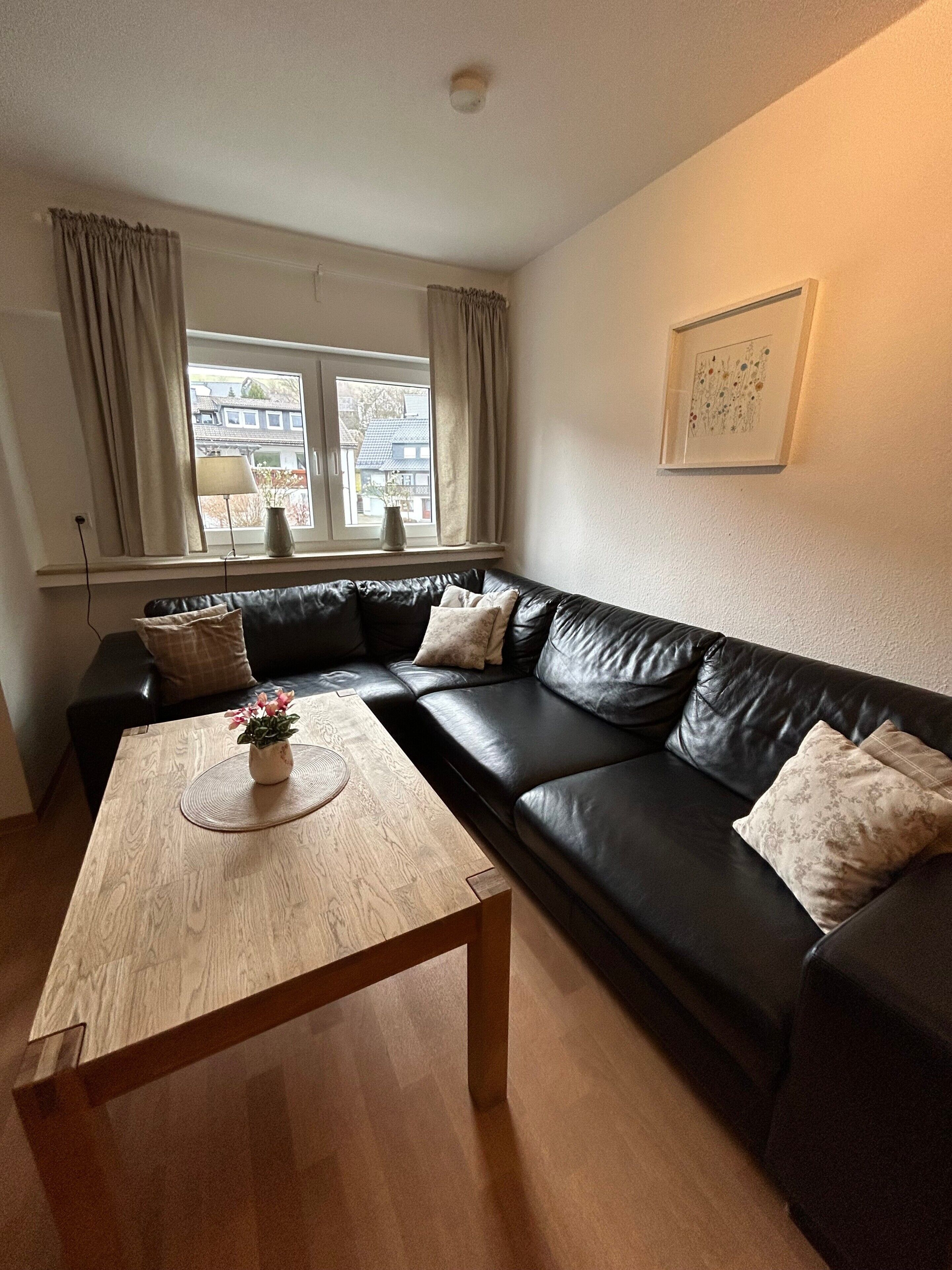 A living room with a black leather sofa, a wooden coffee table, and a window with curtains.