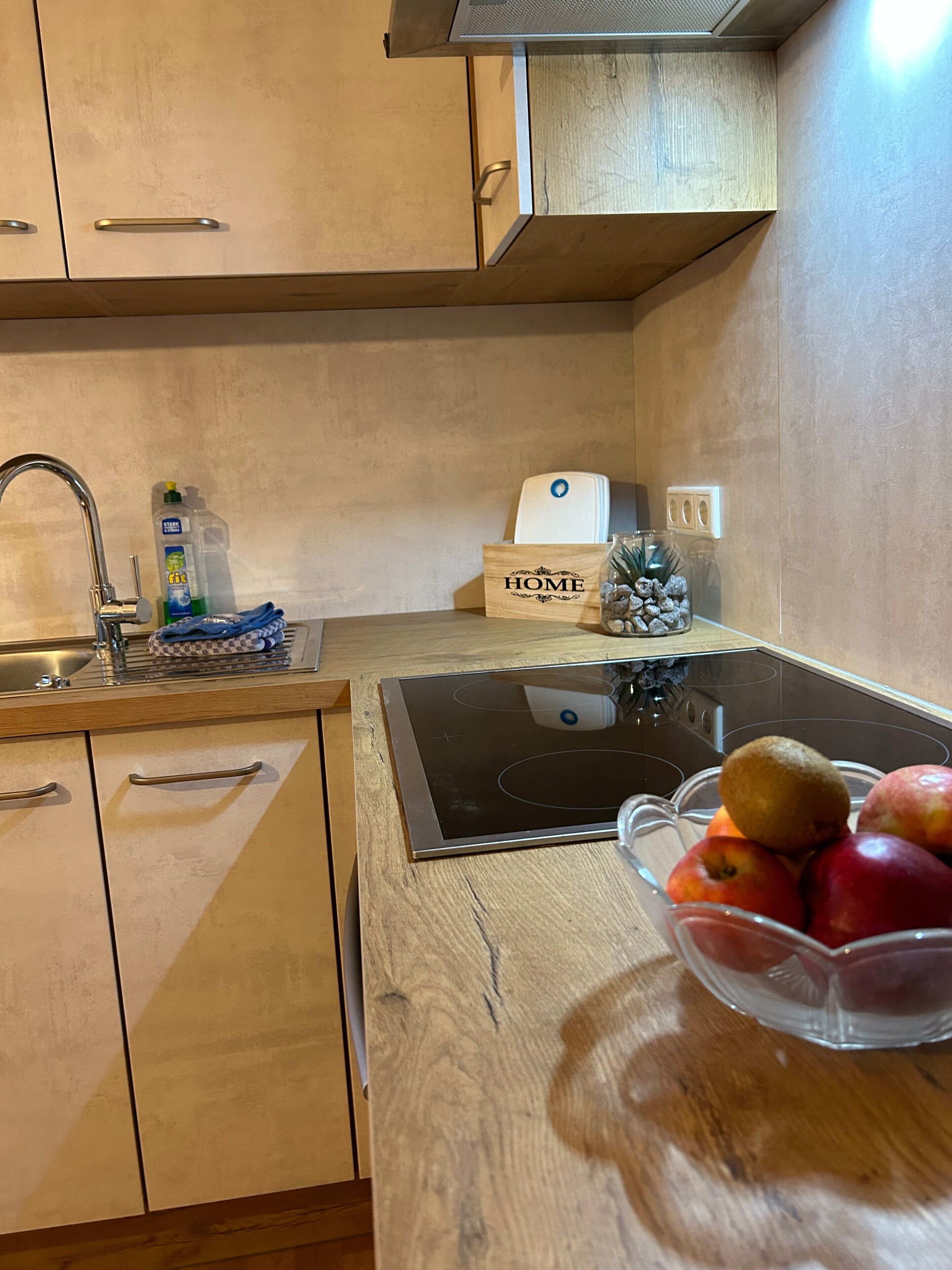 Une cuisine avec des meubles de rangement en bois, un évier, une cuisinière et un saladier rempli de fruits posé sur le comptoir.