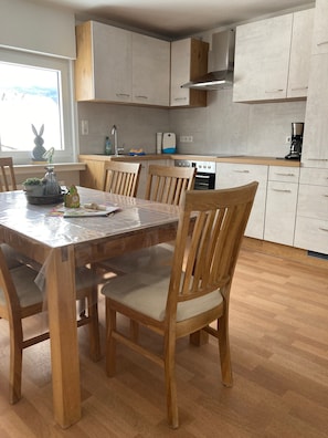 A modern kitchen with wooden cabinets, a dining table with chairs, and a window with a view. - Holiday Apartment '6, 85sqm' with Shared Terrace, Shared Garden and Wi-Fi (Schmallenberg)