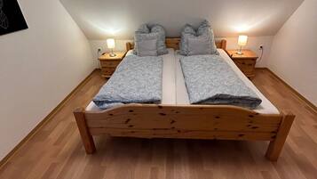 Ein Schlafzimmer mit einem hölzernen Bett, zwei Nachttischen mit Lampen und einer weißen Wand mit einem schwarzen Kunstwerk.
