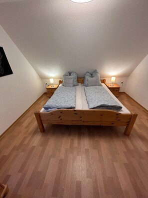 A bedroom with a wooden bed, two bedside tables with lamps, and a white wall with a black artwork. - Holiday Apartment '6, 85sqm' with Shared Terrace, Shared Garden and Wi-Fi (Schmallenberg)