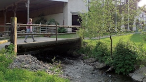 A building with a covered outdoor area, a bridge over a stream, and a person walking. - Holiday Apartment '7, 70sqm' with Shared Terrace, Shared Garden and Wi-Fi (Schmallenberg)