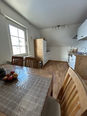 A compact kitchen with a dining area, wooden chairs, a table with a plaid tablecloth, and a window with a view.