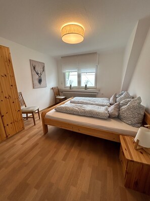 A bedroom with a wooden bed, a chair, a radiator, and a window with blinds. - Holiday Apartment '7, 70sqm' with Shared Terrace, Shared Garden and Wi-Fi (Schmallenberg)