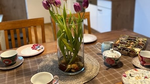 A dining table with a vase of purple tulips, a placemat, and various tea cups and saucers. - Holiday Apartment '7, 70sqm' with Shared Terrace, Shared Garden and Wi-Fi (Schmallenberg)