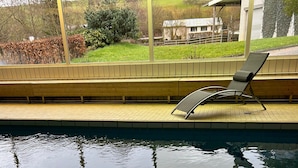 A swimming pool with a tiled edge, a lounge chair, and a view of a house and trees. - Holiday Apartment '7, 70sqm' with Shared Terrace, Shared Garden and Wi-Fi (Schmallenberg)