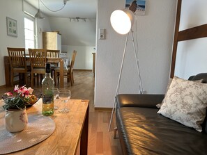 A living room with a sofa, a dining table with chairs, a floor lamp, and a wall-mounted picture.