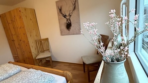 A bedroom with a bed, a chair, a wooden wardrobe, a vase with flowers, and a deer head artwork on the wall. - Holiday Apartment '7, 70sqm' with Shared Terrace, Shared Garden and Wi-Fi (Schmallenberg)