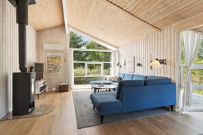 Ein modernes Interieur mit einem blauen Sofa, einem Glastisch, Holzboden, einem schwarzen Herd und einem großen Fenster.