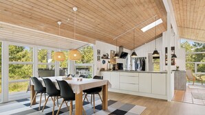 Eine moderne Küche mit Holzausstattung, ein Essbereich mit kariertem Teppich und große Fenster mit Blick auf Grünflächen.