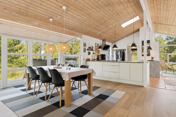 Une cuisine moderne avec des meubles en bois, un coin repas agrémenté d’un tapis à carreaux et de grandes fenêtres donnant sur un paysage verdoyant.