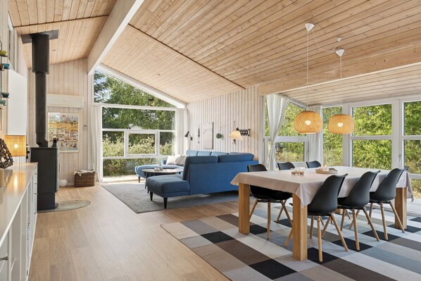 Ein modernes Interieur mit Holzboden, einem blauen Sofa, einem Esstisch mit Stühlen und großen Fenstern.