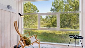 Ein Zimmer mit einem großen Fenster, einem Holzstuhl, einem kleinen Tisch und einer Lampe.