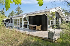 Une maison moderne dotée d’un patio couvert, d’un coin repas avec des meubles en osier et d’une grande fenêtre donnant sur la terrasse.
