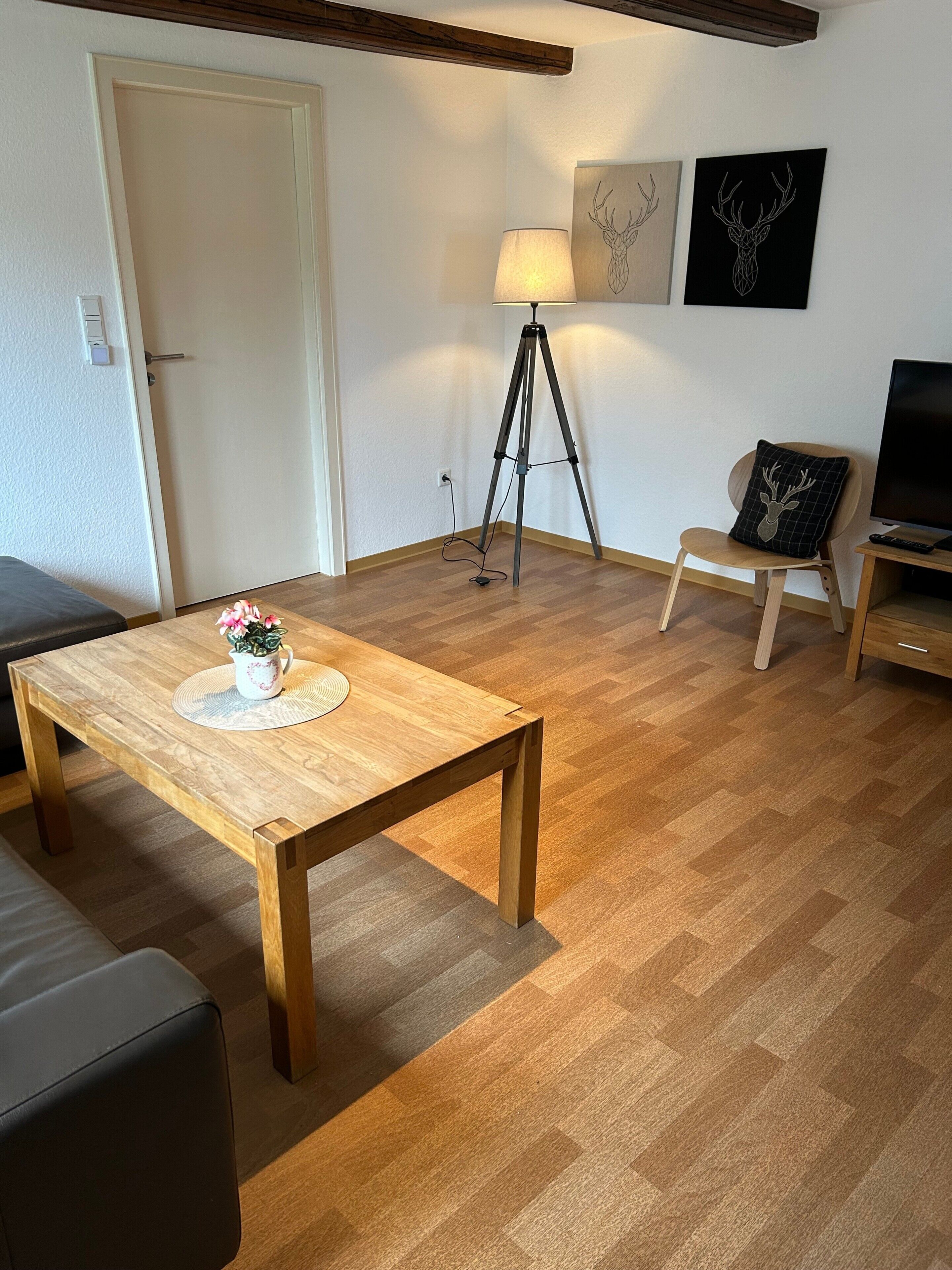 Uma sala de estar com uma mesa de madeira, uma luminária, uma cadeira, um sofá e uma televisão.