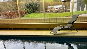 A swimming pool with a tiled edge, a lounge chair, and a view of a house and trees. - Holiday Apartment '1, 70sqm' with Shared Terrace, Shared Garden and Wi-Fi (Schmallenberg)