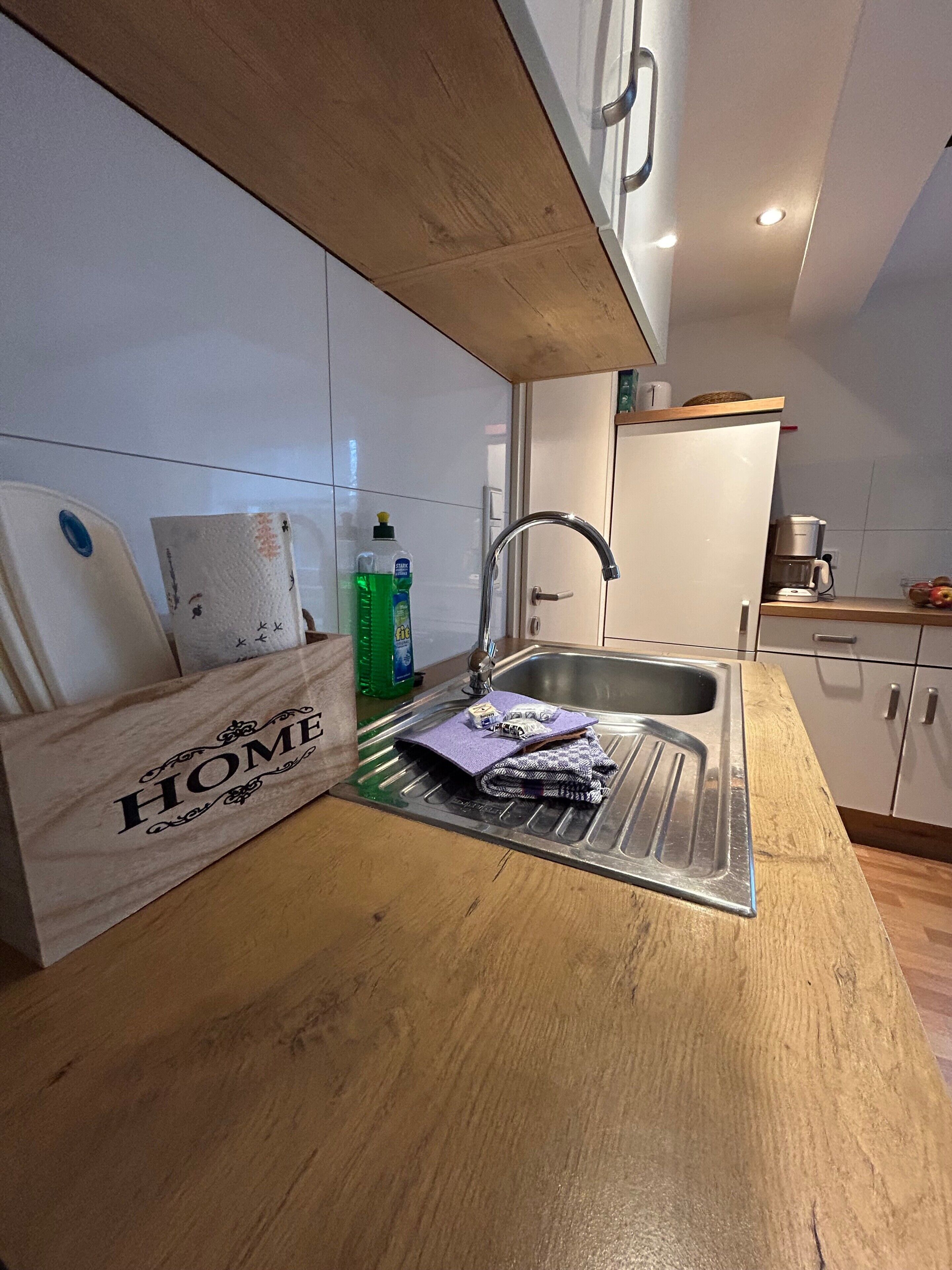 Eine Küche mit Spüle aus Edelstahl, einer Holzausziehtafel, einer Kaffeemaschine und einem Schrank mit Griff.