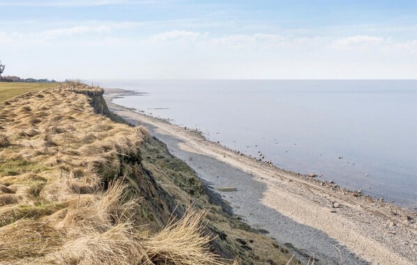 Ett kustlandskap med en gräsklädd klippa, en stenstrand och ett lugnt hav.