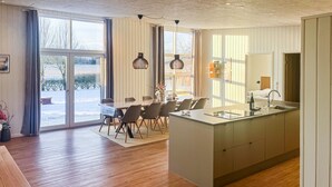 Une cuisine moderne dotée d’un îlot central, de grandes fenêtres et d’un coin repas avec des chaises et une table.